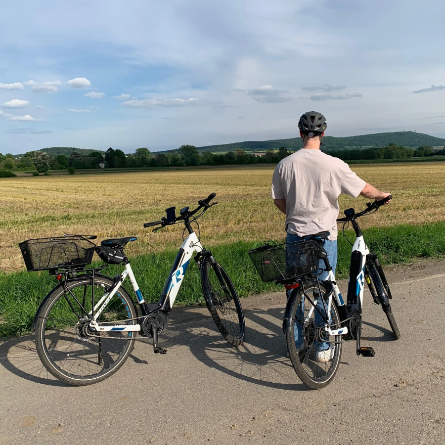 Zwei CityRay E-bikes Fahrräder auf dem Radweg. Mänliche Person hält sich am Lenkrad fest. Preson Steht neben dem E-bike.